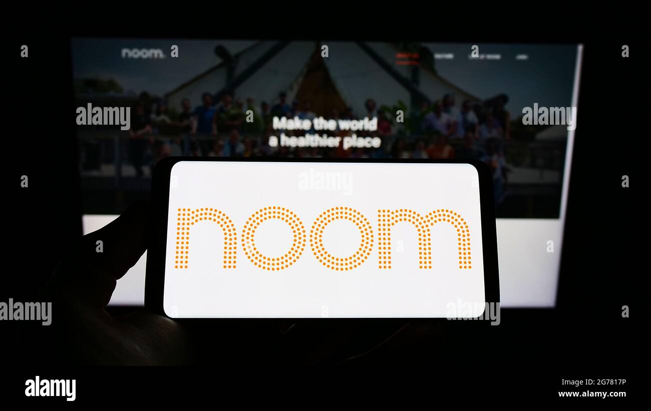 Person holding mobile phone with logo of American weight-loss platform company Noom Inc. on screen in front of web page. Focus on phone display. Stock Photo