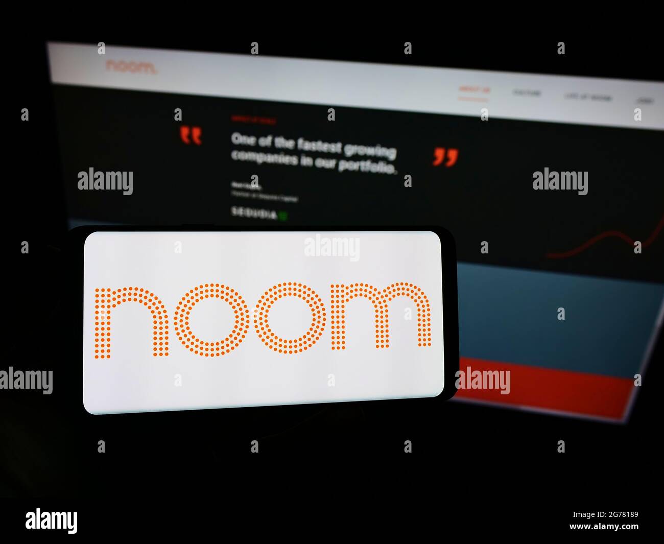 Person holding cellphone with logo of US weight-loss platform company Noom Inc. on screen in front of business webpage. Focus on phone display. Stock Photo