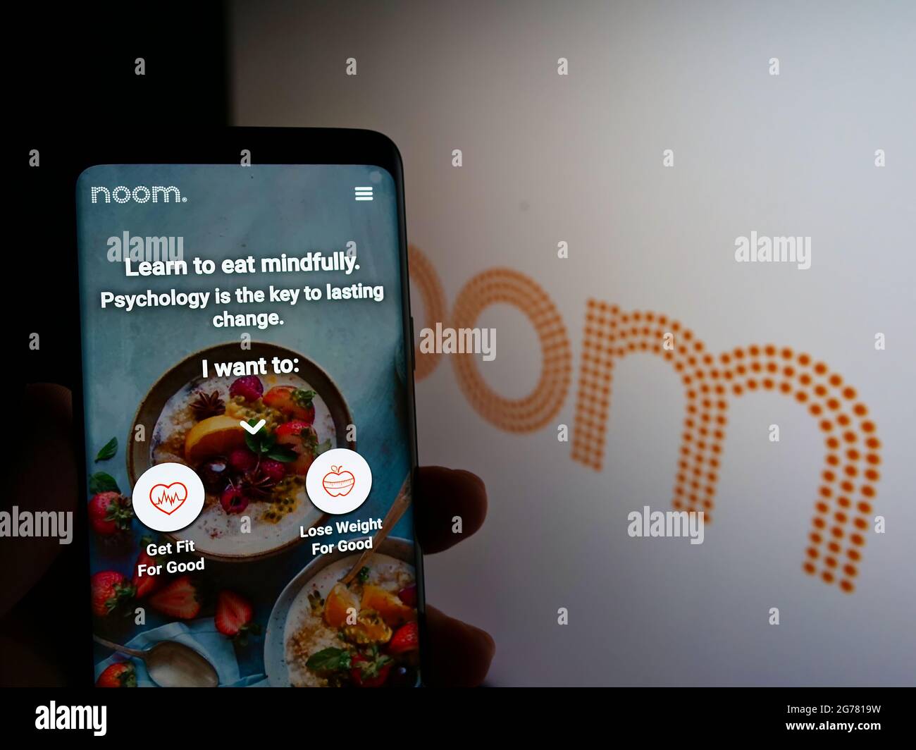 Person holding mobile phone with website of US weight-loss platform company Noom Inc. on screen in front of logo. Focus on center of phone display. Stock Photo