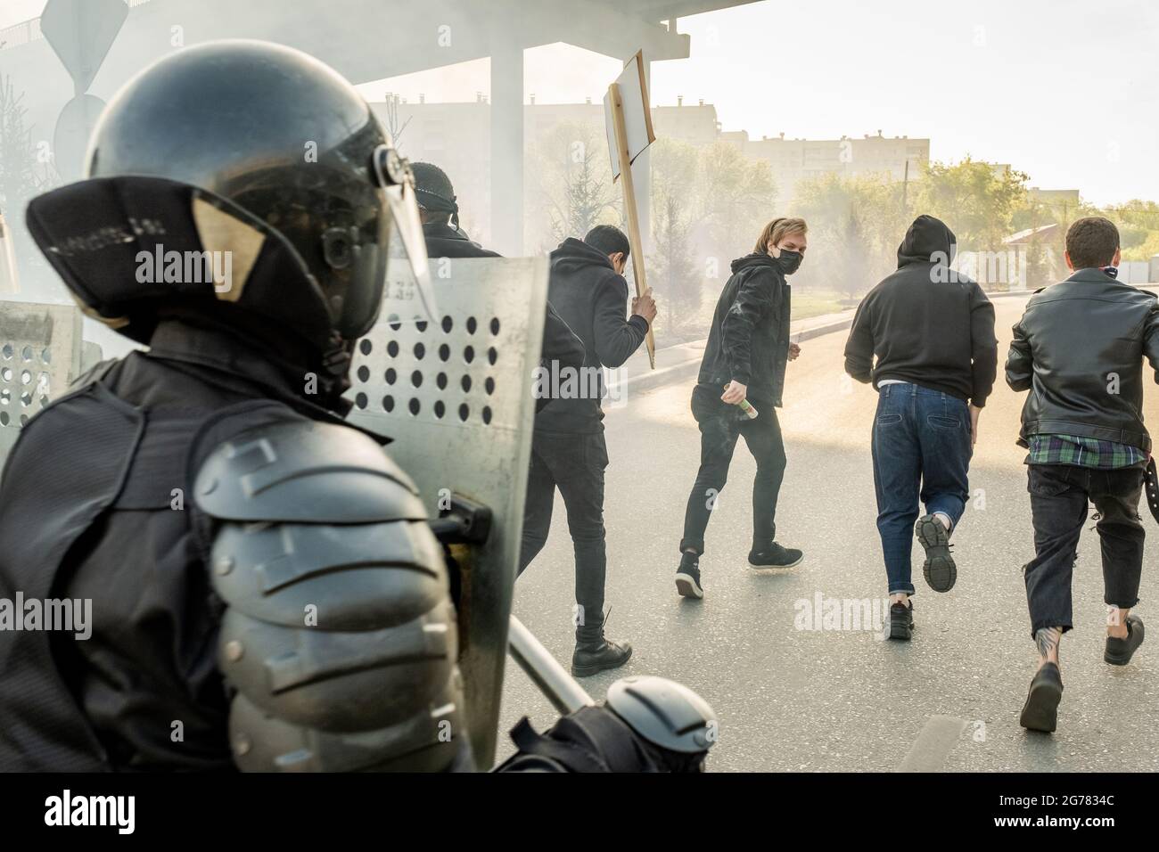 Police forces in helmets holding riot shields moving to running hooligans while stopping them in city Stock Photo