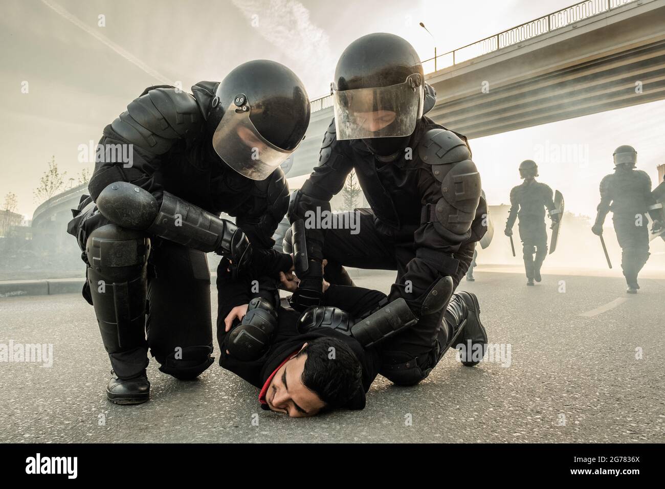 Strong riot policeman in helmets twisting arms of protester behind his back while arresting him on street Stock Photo