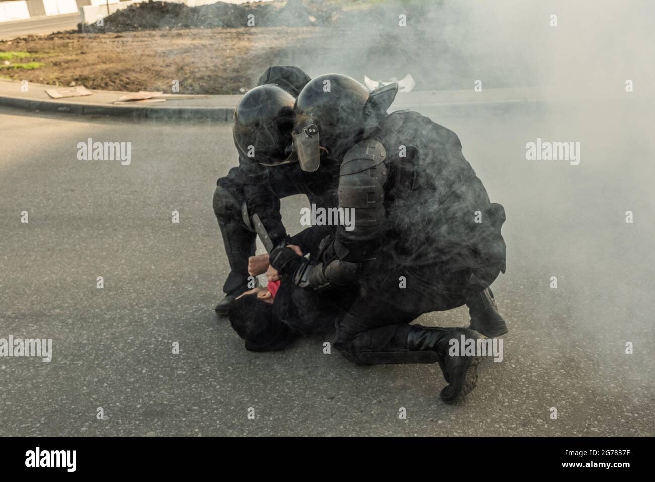 Strong riot police in camouflage outfits putting rebel on ground while using force against him on street Stock Photo