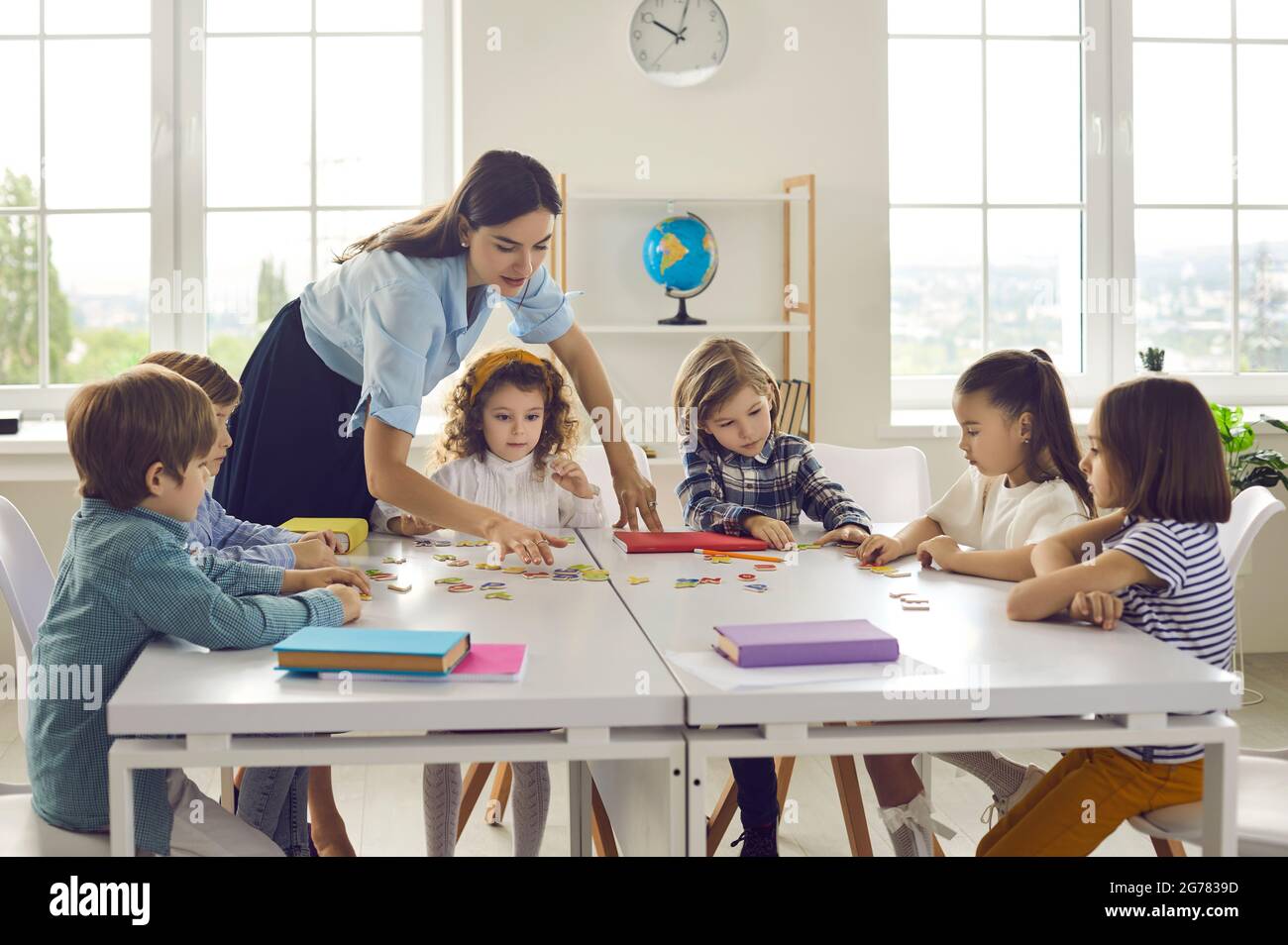 Teacher helping little primary school children group join puzzle in ...