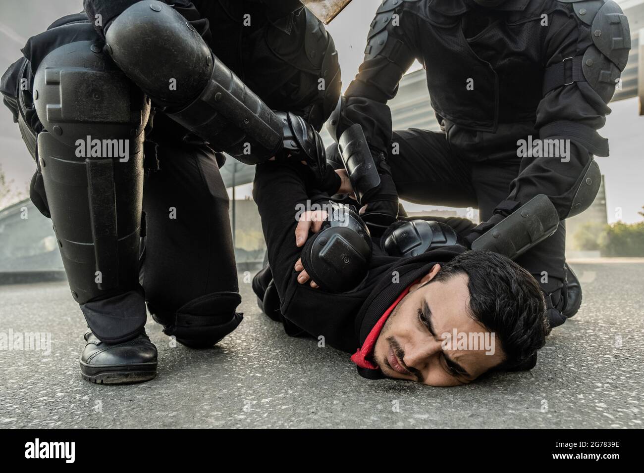 Riot force in protective wear pressing middle eastern man to ground while rresting him during rally Stock Photo
