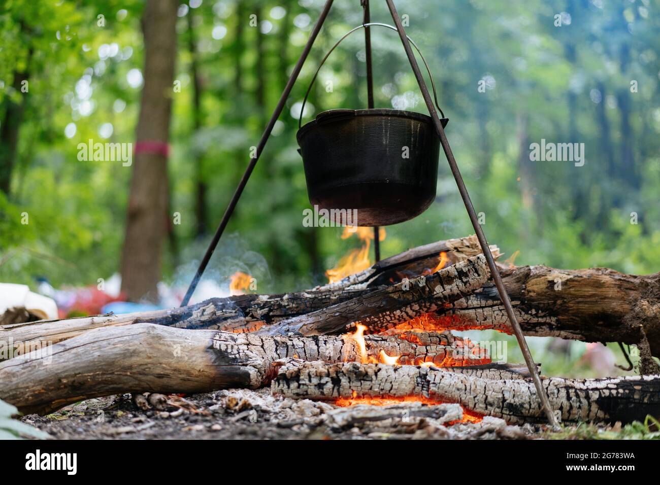 Over the fire hangs a pot in which to cook food. On a hook on a tripod,  steam comes out of the pan. Winter Camping outdoor cooking Stock Photo -  Alamy