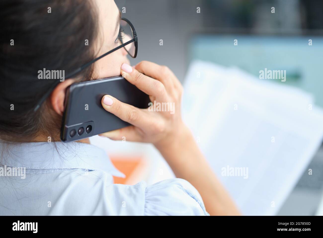 Businesswoman talking on smartphone and reading document solving corporate business problems Stock Photo