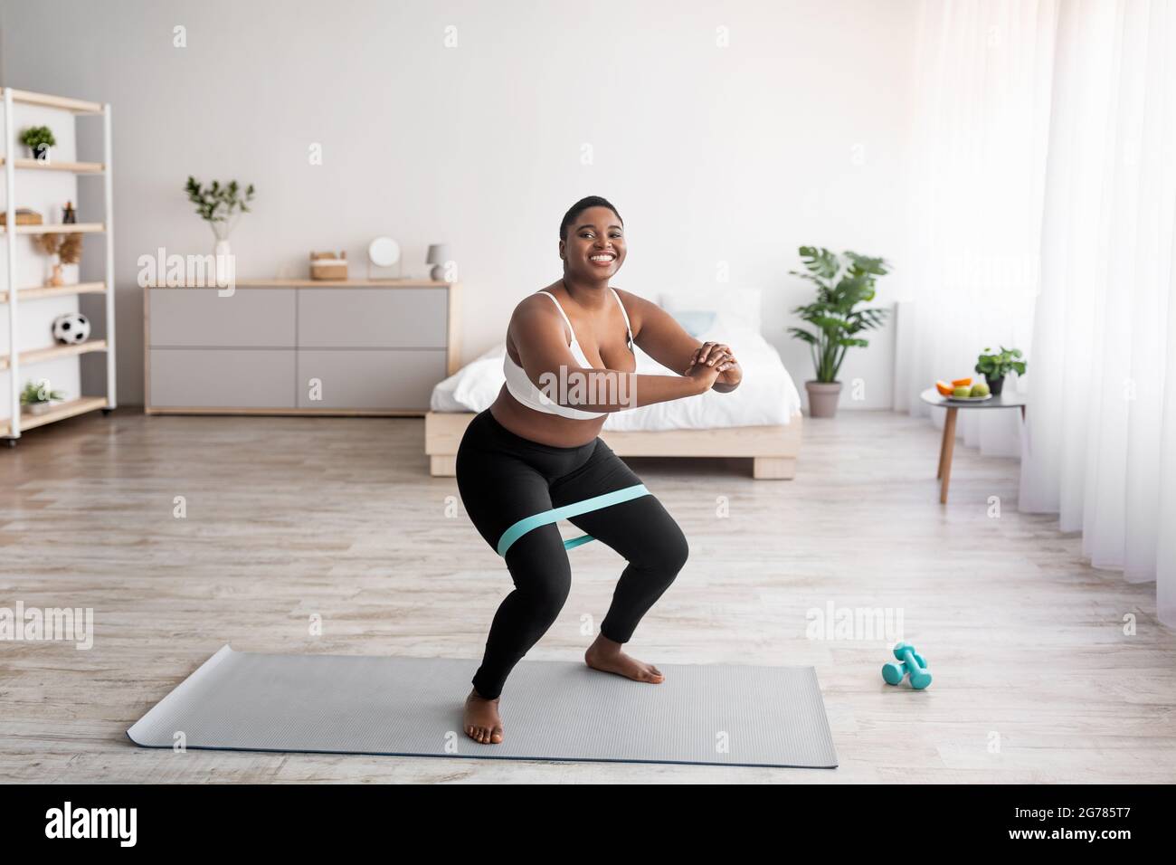Full Length Of Curvy Black Woman Squatting With Elastic Band During Home Workout Copy Space
