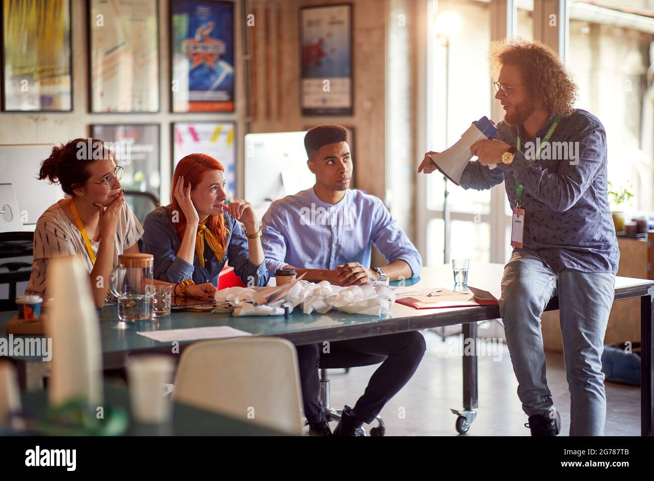 A young man is having fun while giving orders by megaphone to his colleagues in a cheerful atmosphere in the office Stock Photo