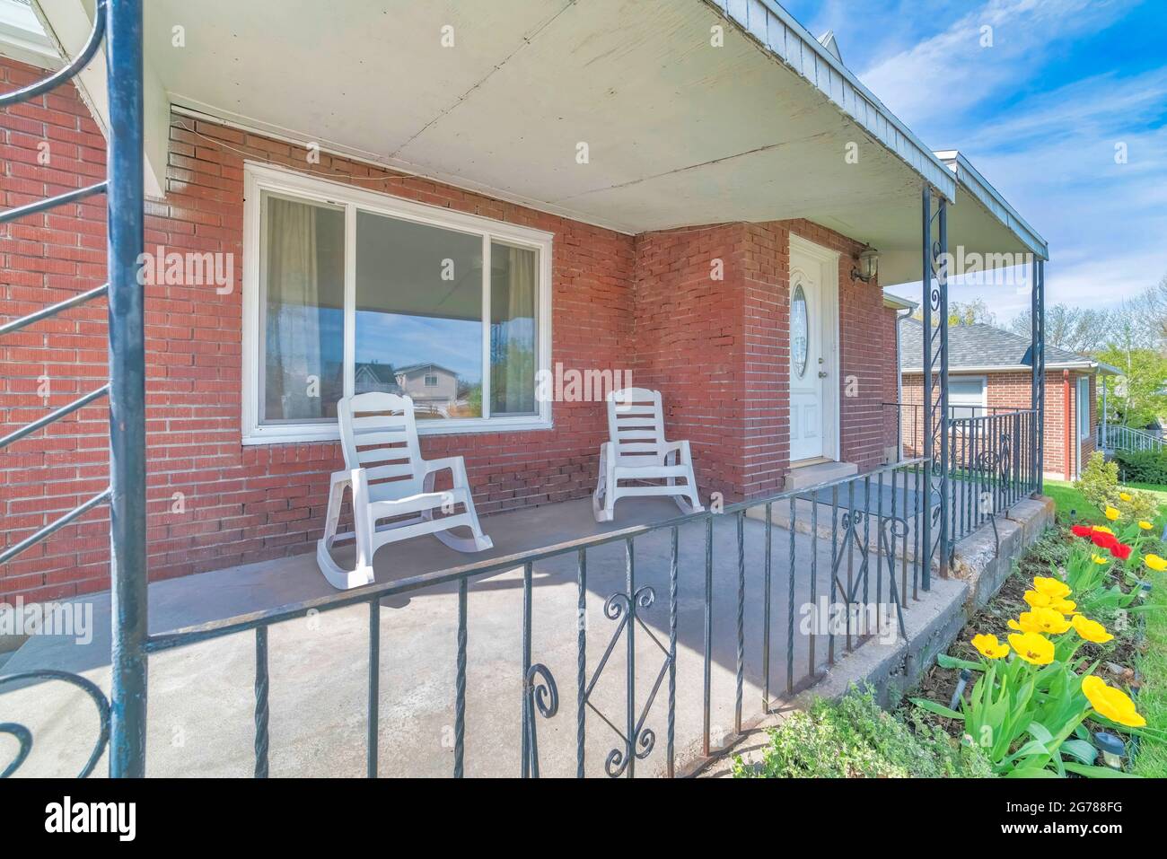 Rocking chairs on the front porch of a house with red brick wall and white door Stock Photo