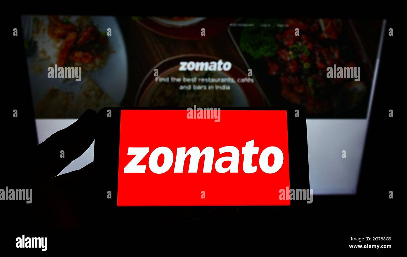 Person holding smartphone with logo of Indian online food ordering company Zomato on screen in front of website. Focus on phone display. Stock Photo