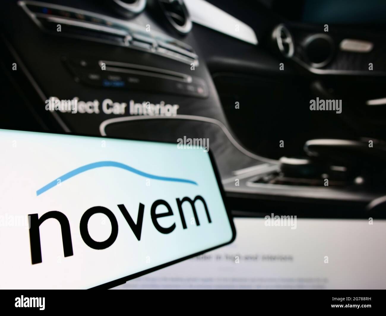 Cellphone with logo of German automotive supplier Novem Car Interior Design on screen in front of website. Focus on center-left of phone display. Stock Photo