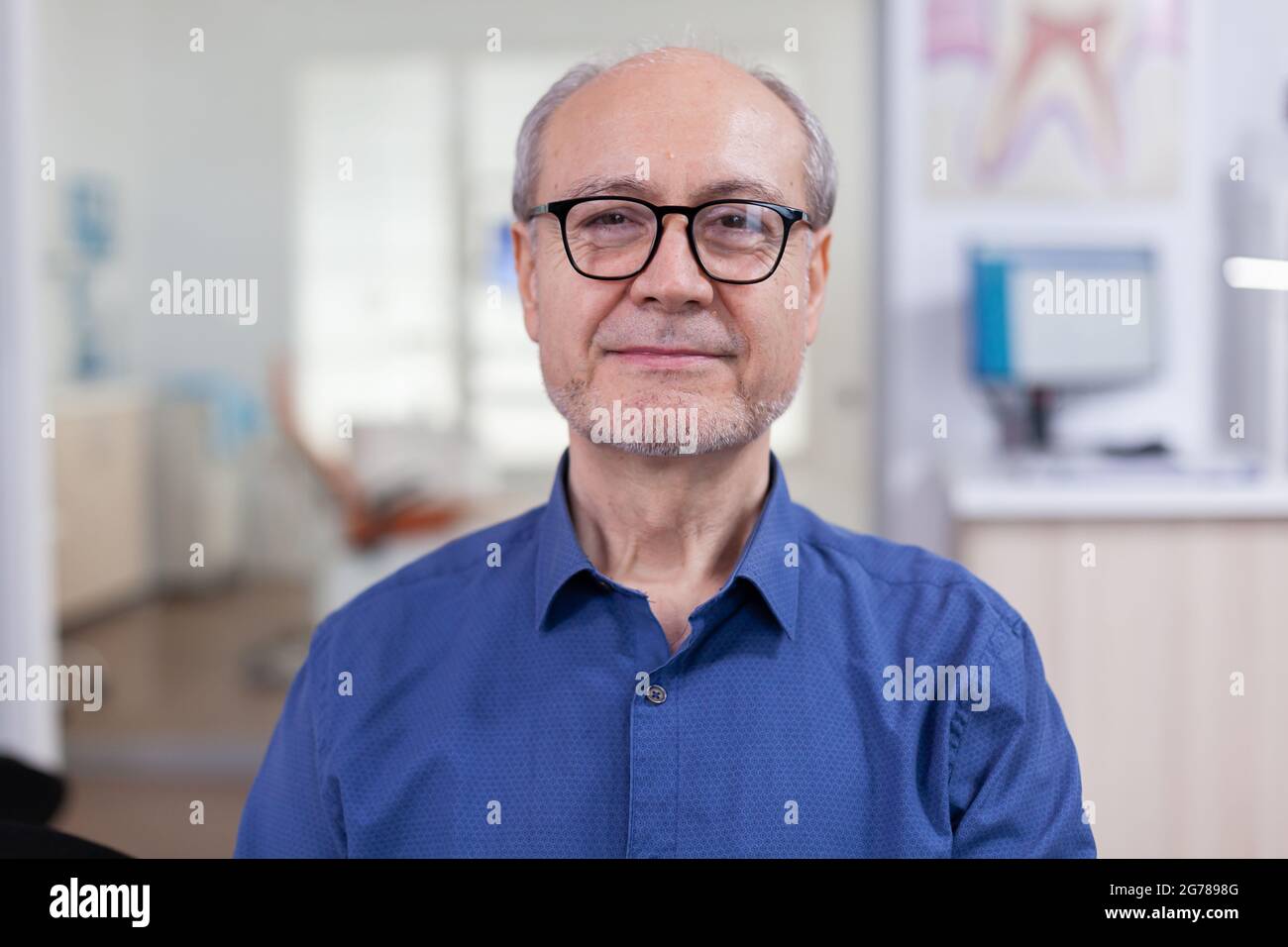 Senior man looking at camera in dental office wainting consultation. Elderly male smiling on webcam sitting on chair in waiting room of stomatological clinic, Stock Photo