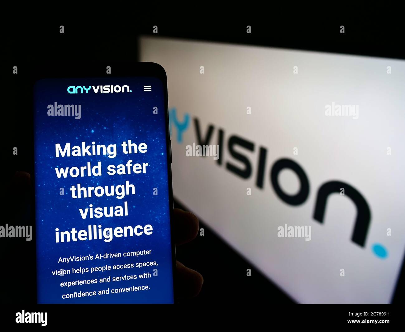 Person holding cellphone with website of company AnyVision Interactive Technologies on screen in front of logo. Focus on center of phone display. Stock Photo