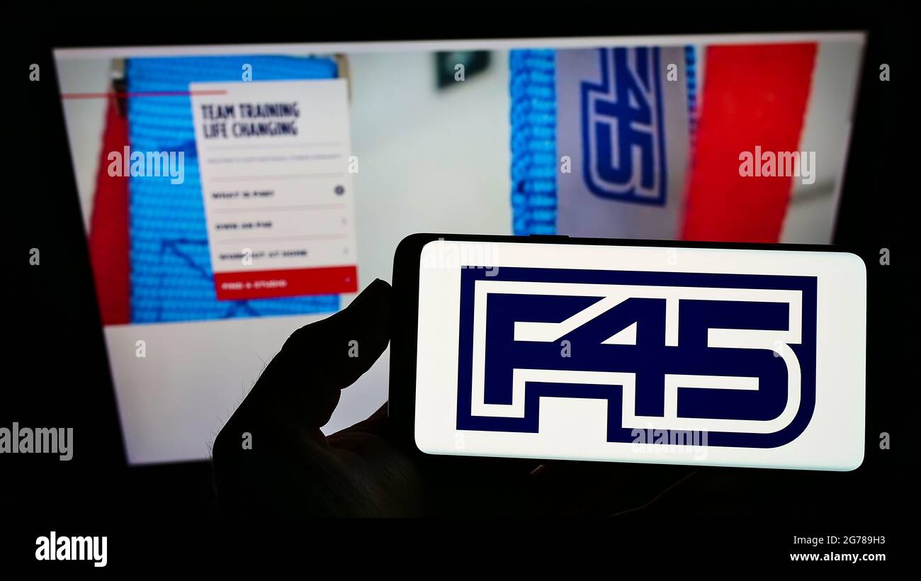 Person holding smartphone with logo of fitness company F45 Training Holdings Inc. on screen in front of website. Focus on phone display. Stock Photo