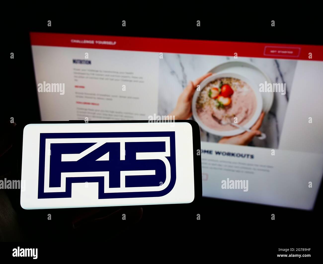 Person holding mobile phone with logo of fitness company F45 Training Holdings Inc. on screen in front of web page. Focus on phone display. Stock Photo