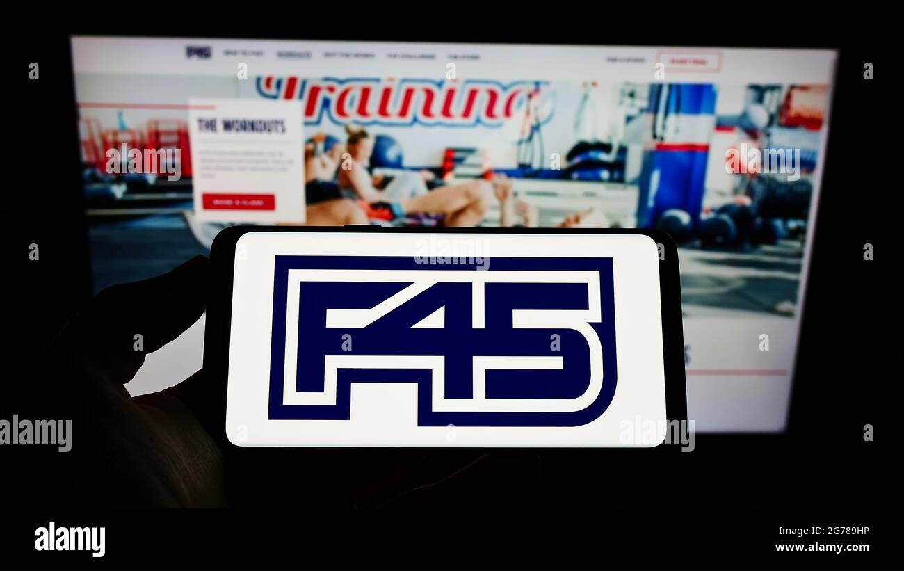 Person holding cellphone with logo of fitness company F45 Training Holdings Inc. on screen in front of business webpage. Focus on phone display. Stock Photo