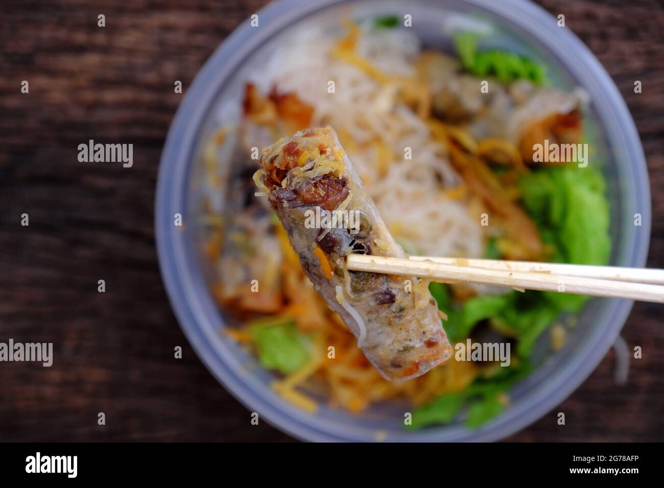 Top view close up hand hold chopsticks pick up fried spring rolls on vegan rice noodles serving from order online in plastic bowl Stock Photo