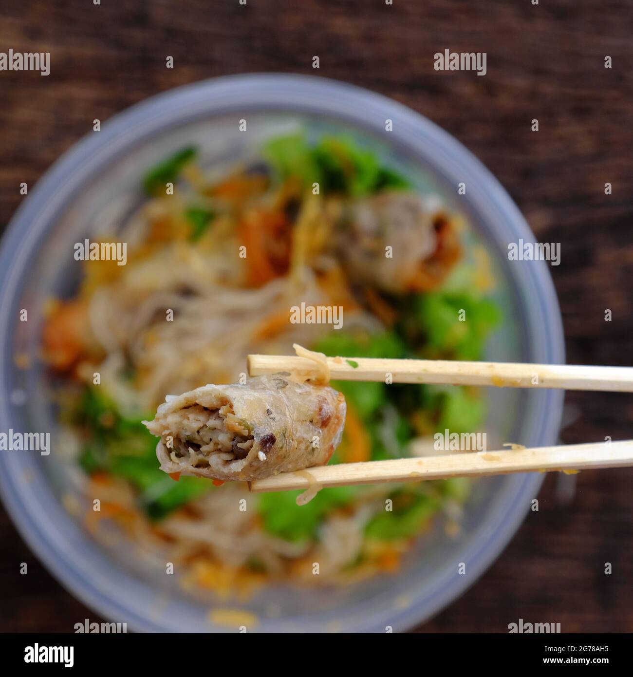 Top view close up hand hold chopsticks pick up fried spring rolls on vegan rice noodles serving from order online in plastic bowl Stock Photo