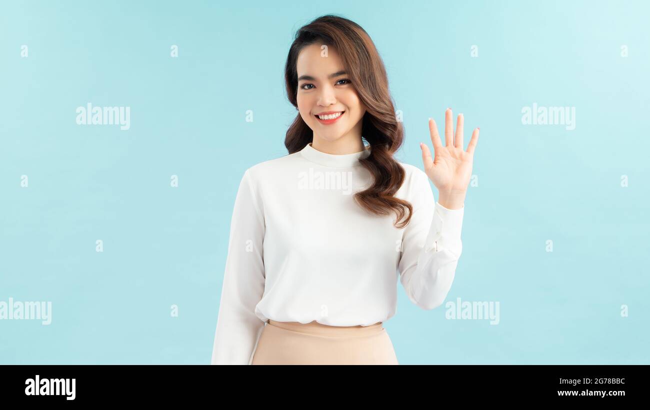 Friendly, pleasant and cheerful east-asian woman raising palm, wave hand greeting, saying hi or hello and smiling with joyful expression as welcoming Stock Photo