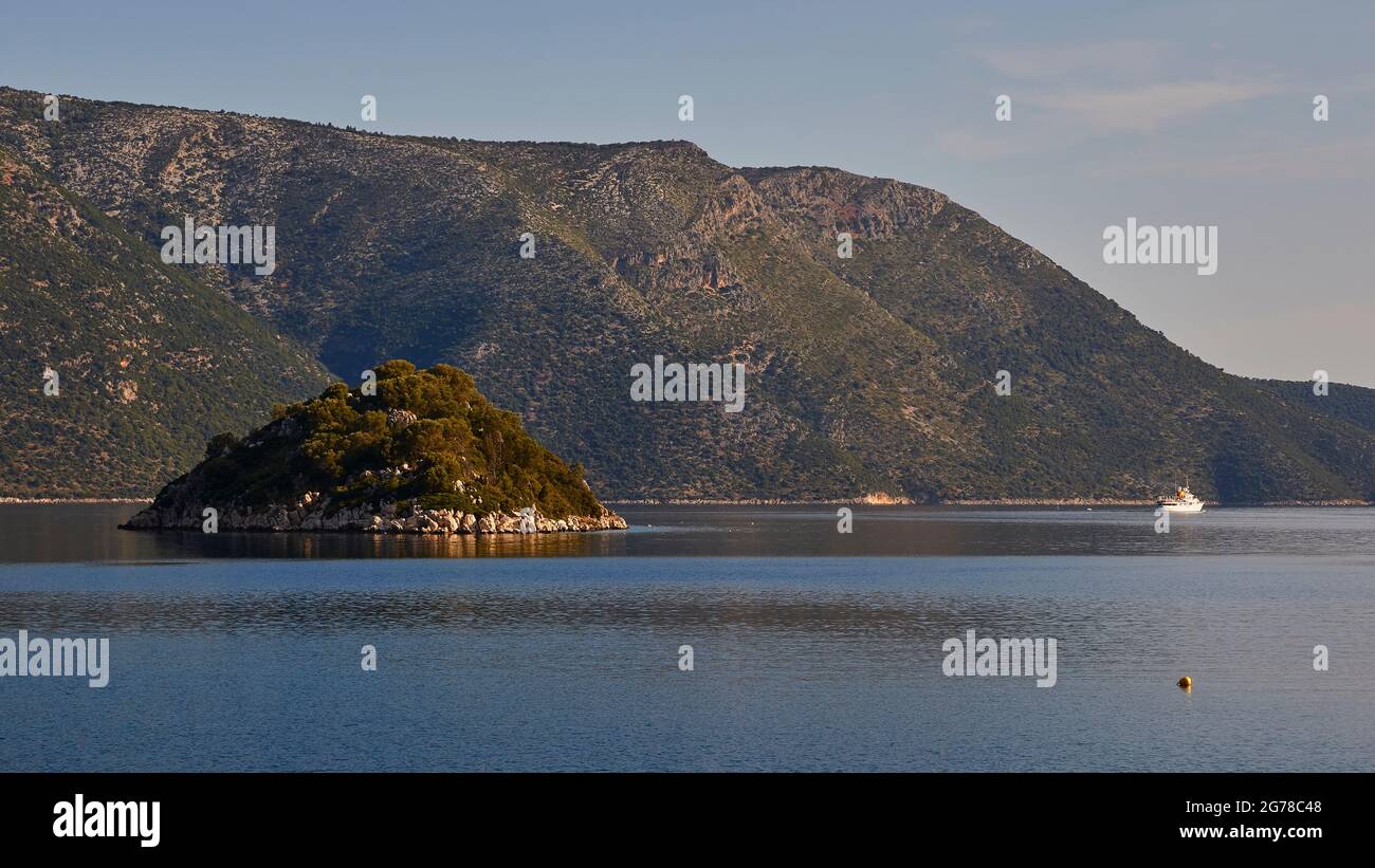 Ionian Islands, Ithaca, island of Odysseus, capital, Vathi, view of the wooded islet Skartsoubonisi in the Bay of Molos, ship on the right in the picture, blue sea, green hills in the background, light blue sky with wispy white clouds Stock Photo