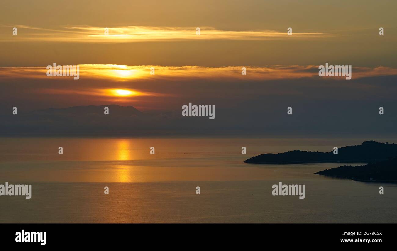 Ionian Islands, Ithaca, Island of Odysseus, Bay of Molos, sunrise, dawn, sun behind cloud bank, sunbeam on the sea, headlands on the right as a silhouette in the picture, mountain ranges of the mainland recognizable in the haze in the background Stock Photo