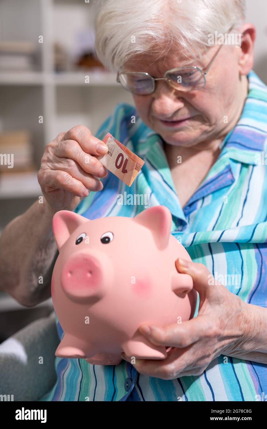Senior woman putting a banknote in a piggy bank Stock Photo - Alamy