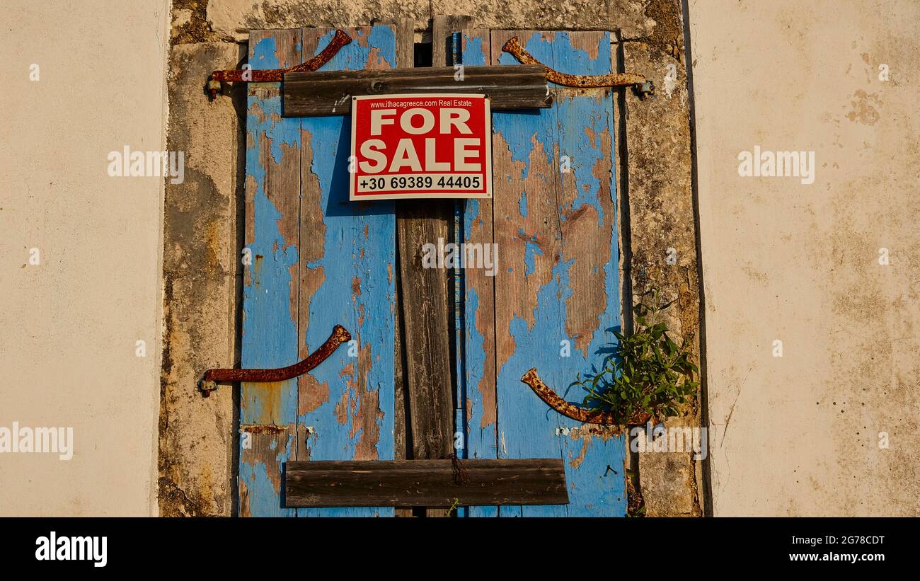 Ionian Islands, Ithaka, island of Odysseus, northwest, mountain village Exogi, weathered blue shutters, white house wall left and right, printed sign saying 'FOR SALE' Stock Photo