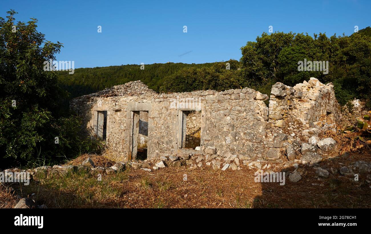 Ionian Islands, Ithaca, island of Odysseus, northwest, mountain village Exogi, ruins of a single standing stone house, behind it forest, blue sky Stock Photo