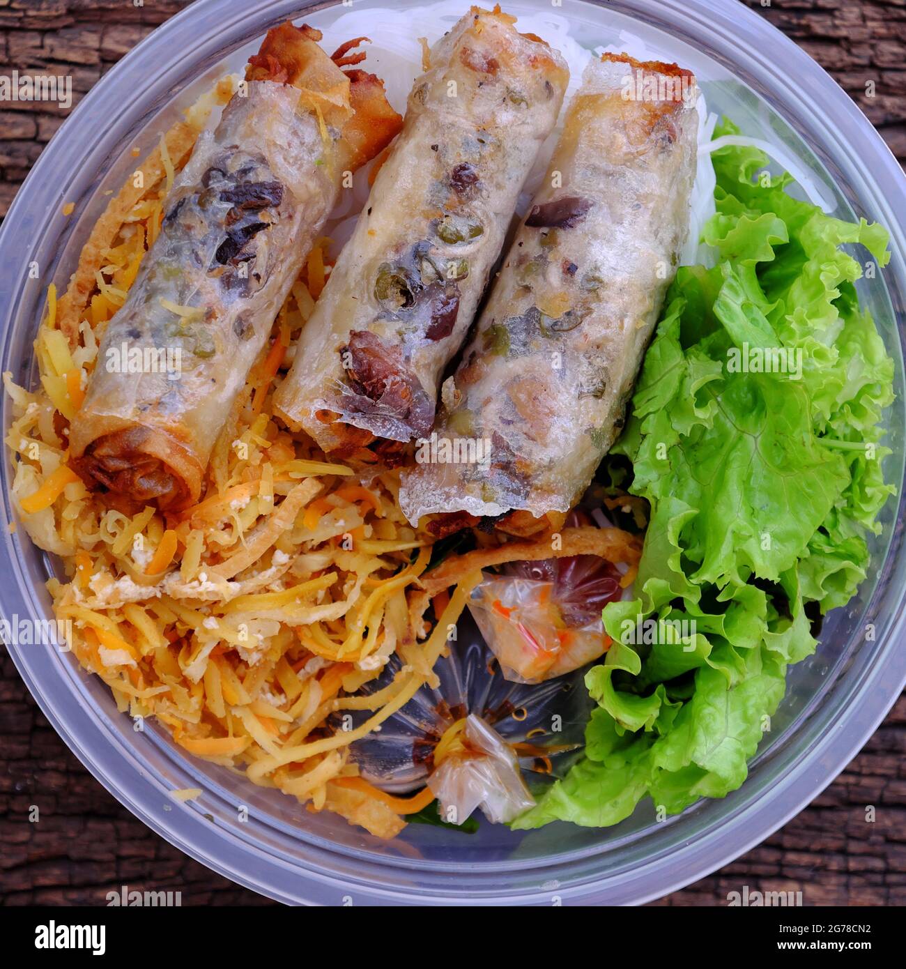 Top view serving from order online in plastic bowl, vegan rice noodles with fried spring rolls and salad, sauce, veg food for Vietnamese vegetarian on Stock Photo