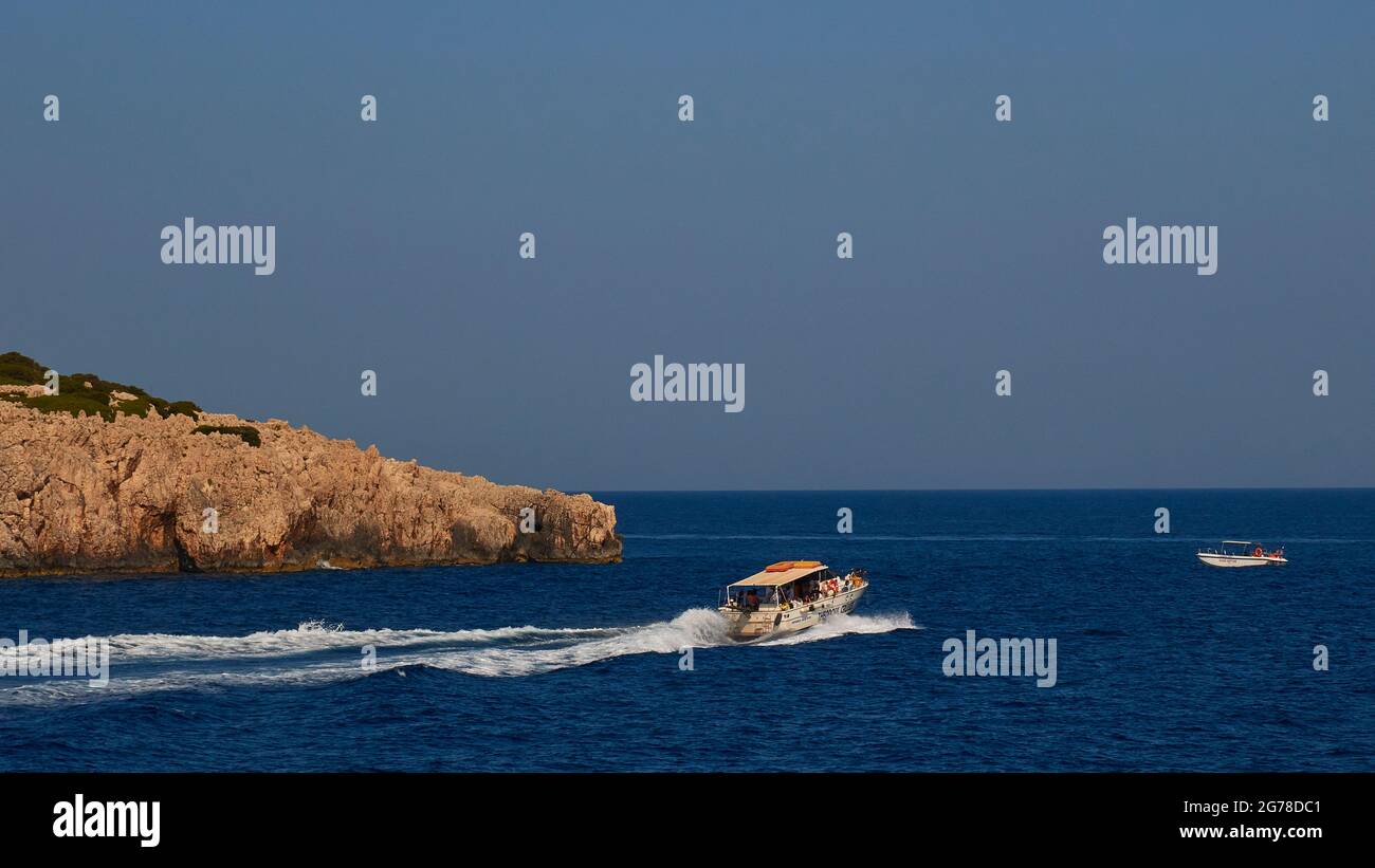 Ionian Islands, Zakynthos, northeast coast, Blue Caves, Blue Grottoes, morning light, rocky coast on the left in the picture, excursion boat drives fast (spray) from left to right, a small boat is anchored on the right in the picture, sea dark blue, sky blue Stock Photo