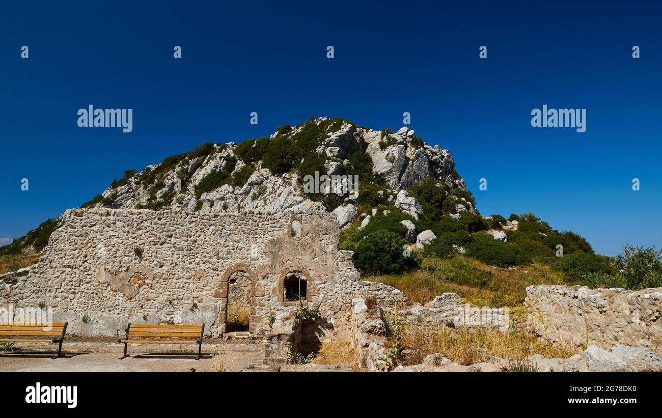 Ionian Islands, Zakynthos, mountain near Zakynthos town, Monte Yves, monastery on the summit, Panagia Skopiotissa, 15th century AD, stands on ruins of an ancient Artemis temple, dark blue sky, stone wall with arched door in the middle distance, Park benches in front of it, rocky peaks in the background Stock Photo