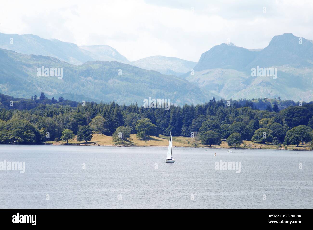 Peaceful Meandering. Lone yacht on Windermere with the Langdale Pikes beyond. Stock Photo