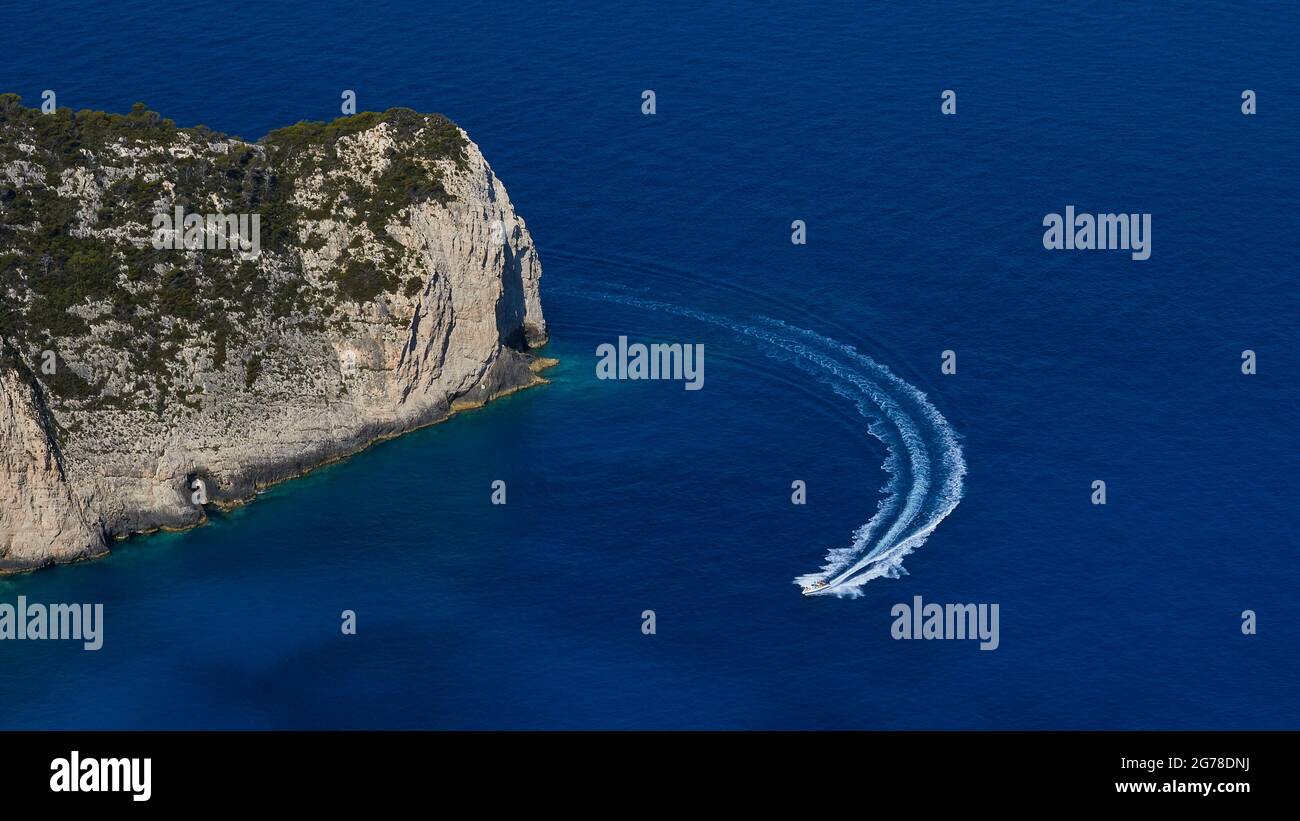 Zakynthos, Paralia Navagio, Shipwreck Beach, view of the northern end of the bay, deep blue water, no sky, excursion boat drives into the bay at high speed Stock Photo