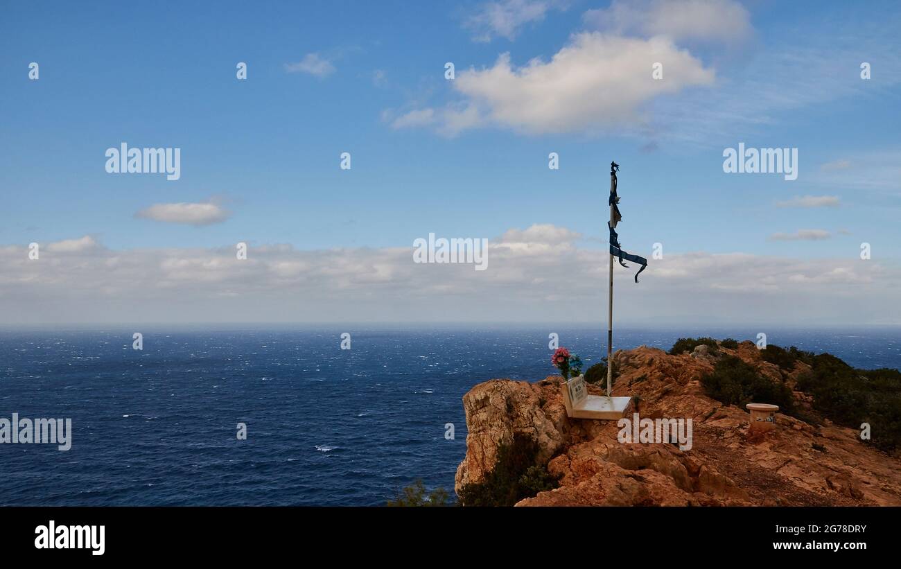 Zakynthos, Paralia Navagio, Shipwreck Beach, viewpoint above the bay, memorial with Greek flag, torn by the wind, deep blue sea, rippled by strong wind, blue sky with white clouds Stock Photo
