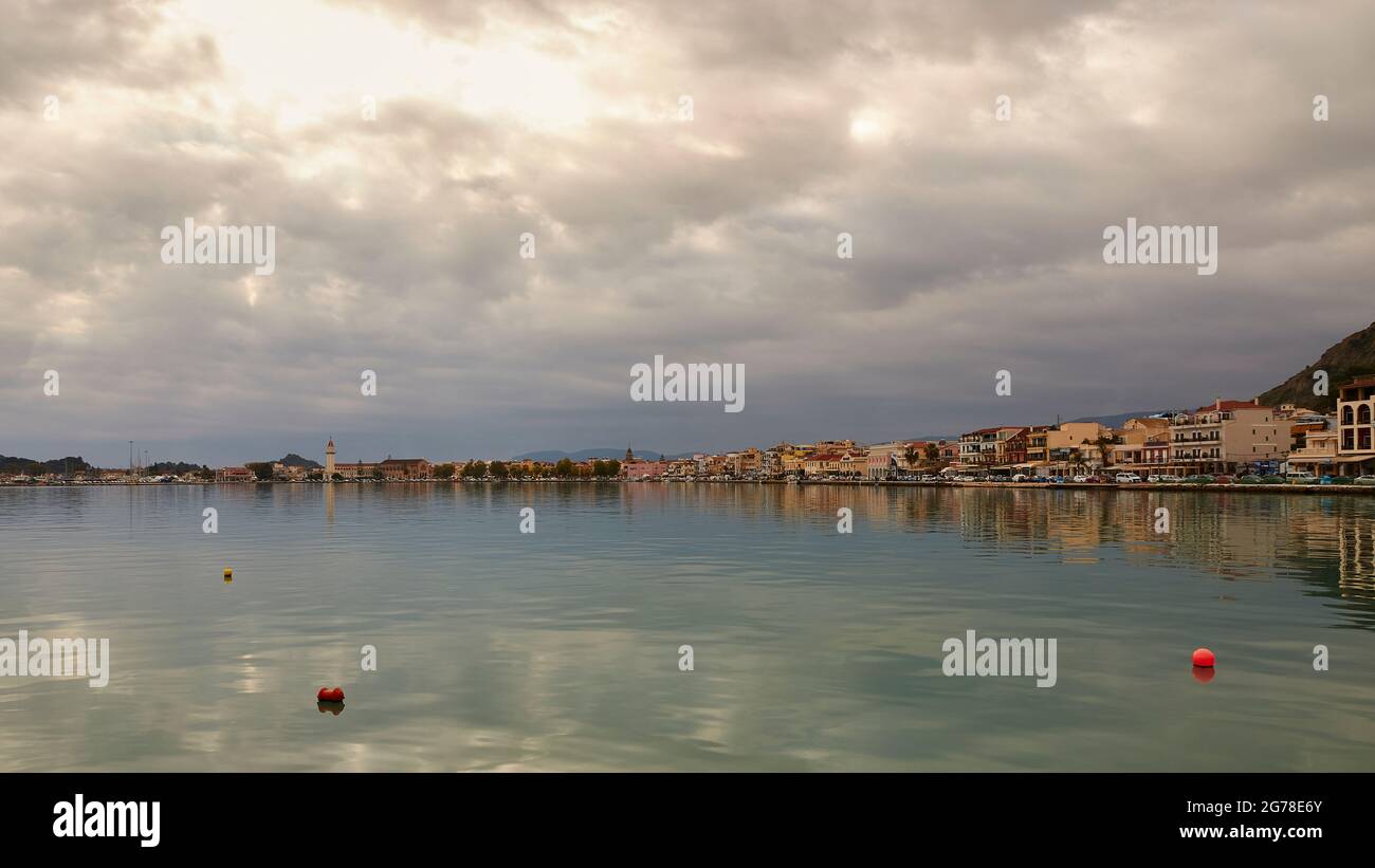 Zakynthos, Zakynthos City, upper 2/3 thick cloud cover through which the sun shines, lower third blue-gray sea, red buoys in the foreground, skyline of Zakynthos City in the middle distance, church tower of Agios Dionysios Church Stock Photo