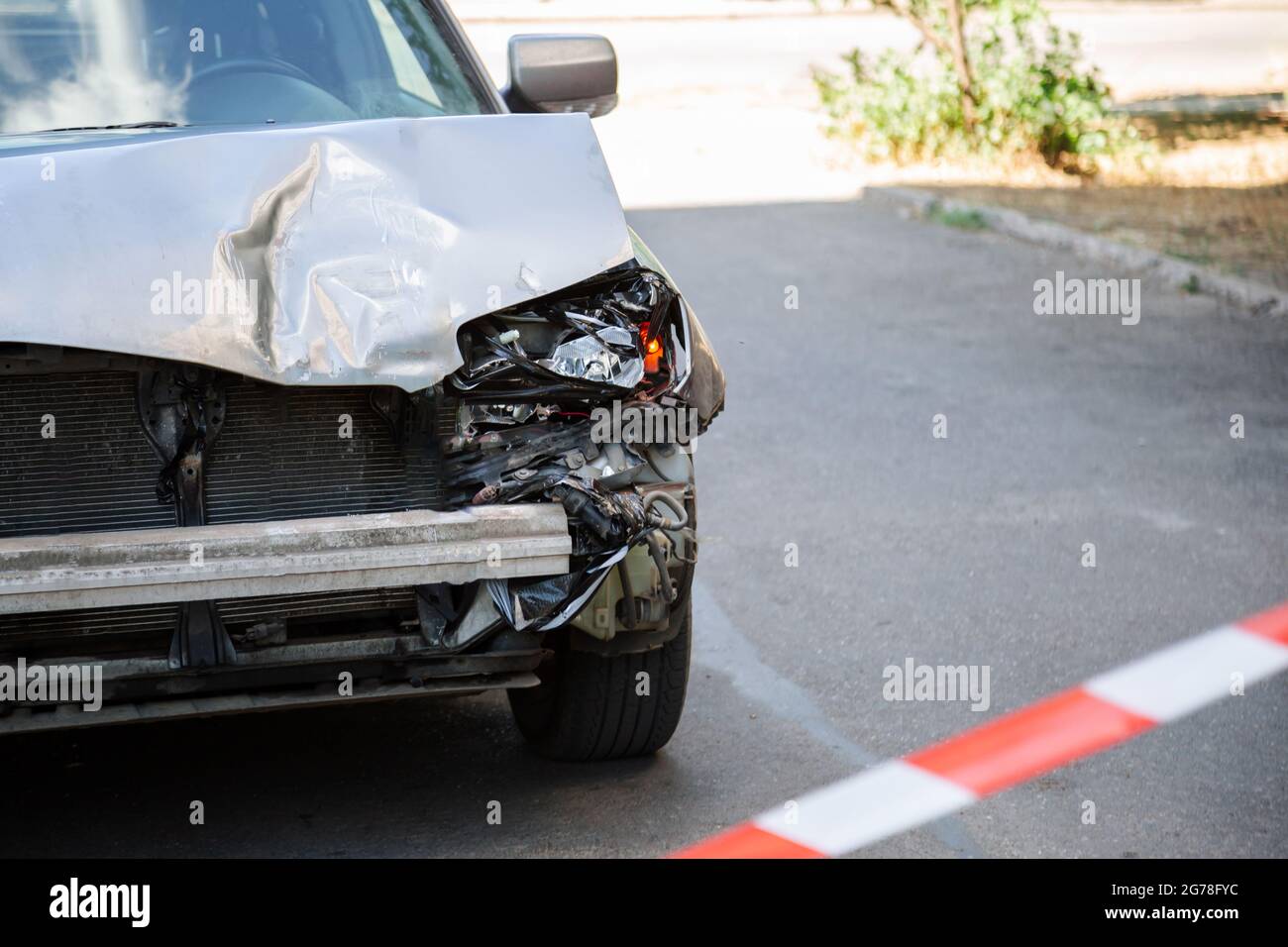 Car accident fenced with red warning tape. Broken hood of car on road. Broken Bumper and Car Headlights with Light On road surface asphalt with copy Stock Photo