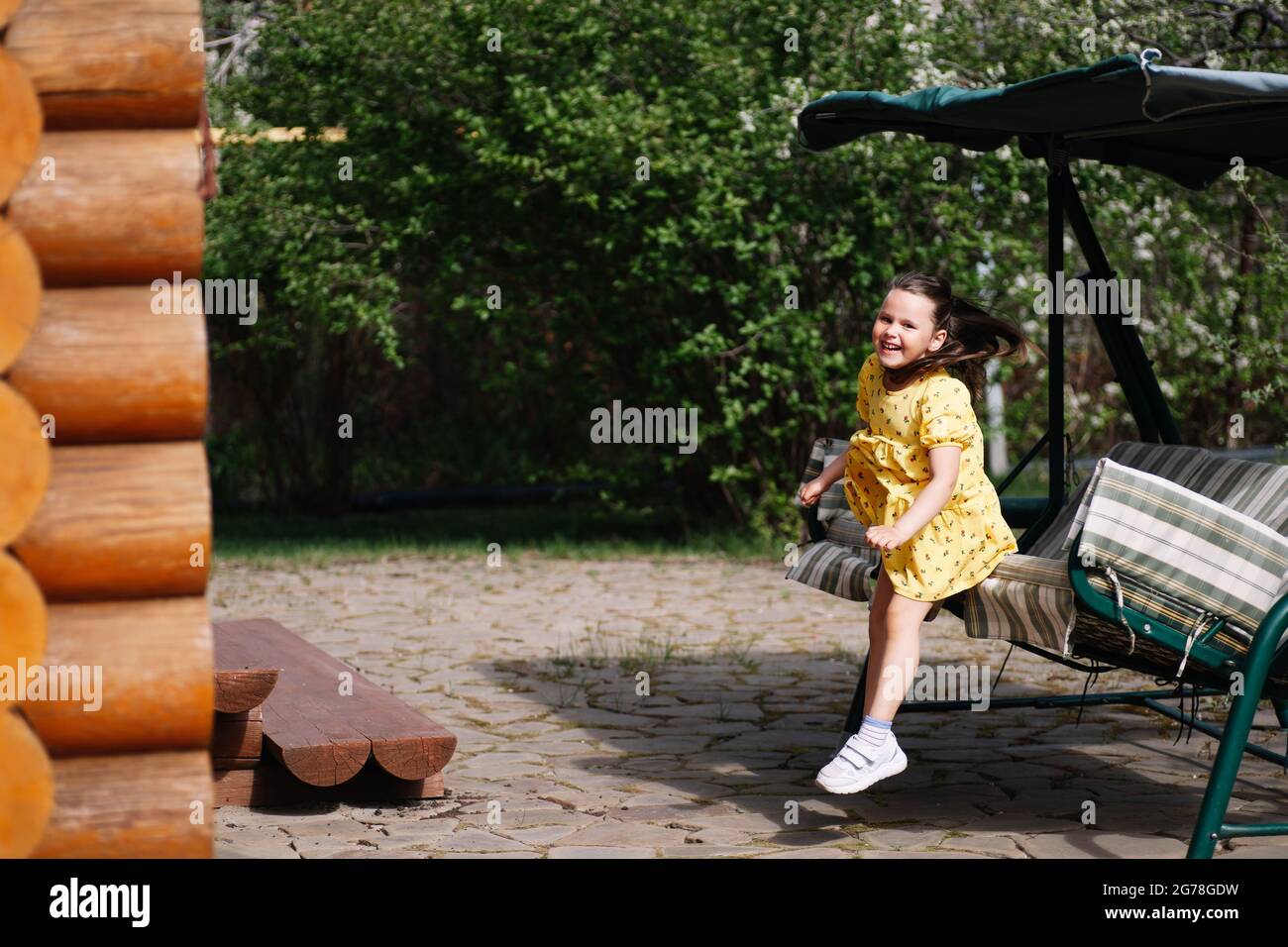 a cheerful, charming girl jumps striped garden in the backyard of a village house on a bright summer day Stock Photo