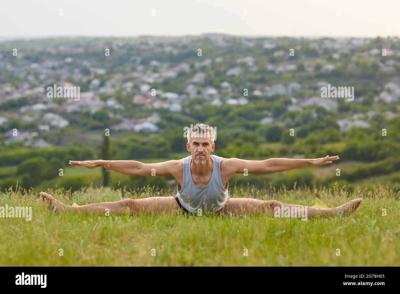 Confident male yogi practicing forward bend and stretching leg exercise in green summer meadow Stock Photo