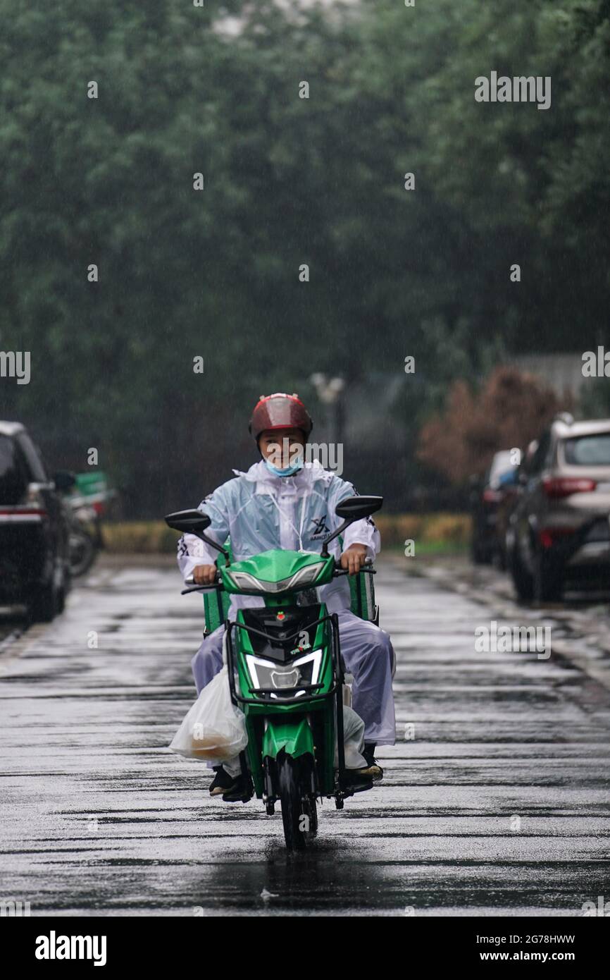 Beijing, China. 12th July, 2021. A deliveryman works on his way in rain in Daxing District of Beijing, capital of China, July 12, 2021. Heavy rainstorm has lashed the Chinese capital Beijing since 6 p.m. Sunday with precipitation up to 116.4 mm, according to the municipal flood control department. From 6 p.m. Sunday to 9 a.m. Monday, Beijing registered average rainfall of 65.9 mm. Urban areas of the city reported higher average precipitation of 79.9 mm. Credit: Peng Ziyang/Xinhua/Alamy Live News Stock Photo