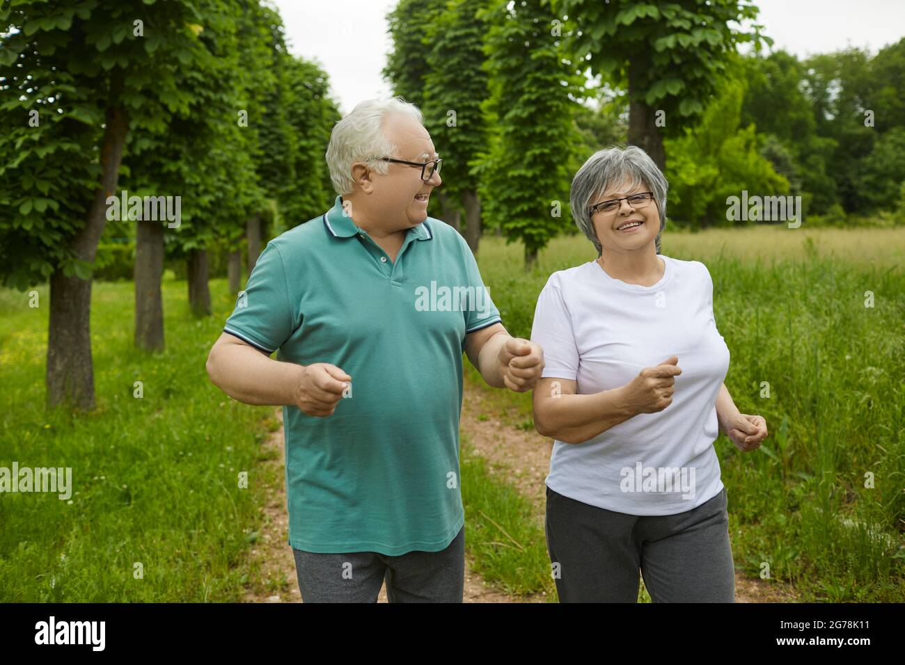 Happy active elderly couple on a summer day jogging outdoors in a park or forest. Stock Photo