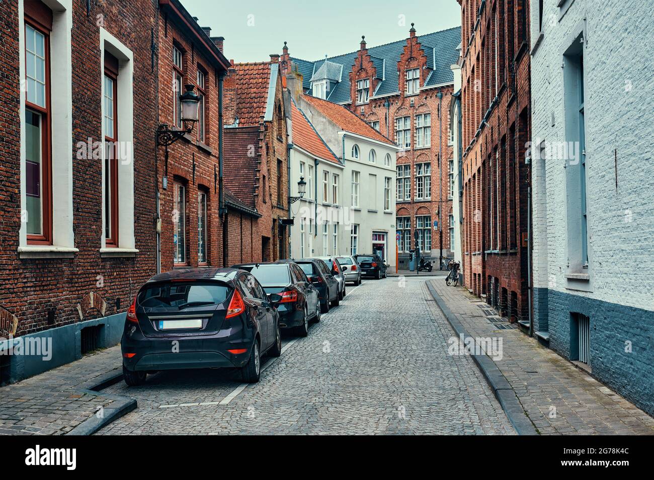 Brugge street with cobblestone road with parked cars and old medieval