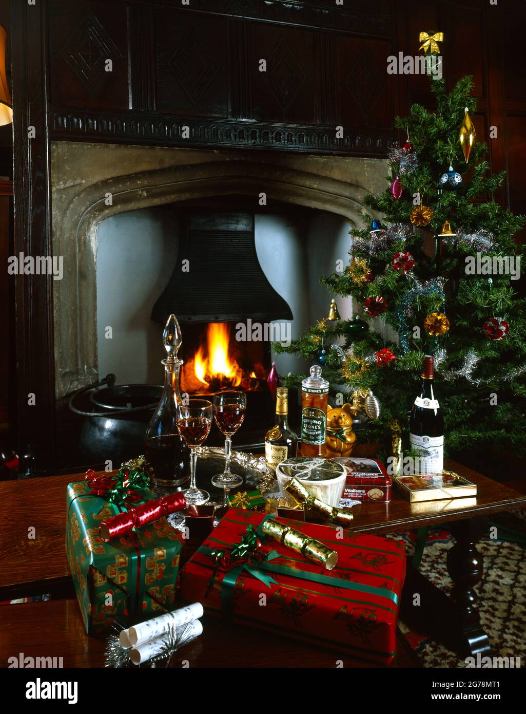 Christmas gifts & produce decorated tree & crackers stone fireplace flames decanter & crystal glasses red wine  brandy wrapped presents copy space Stock Photo