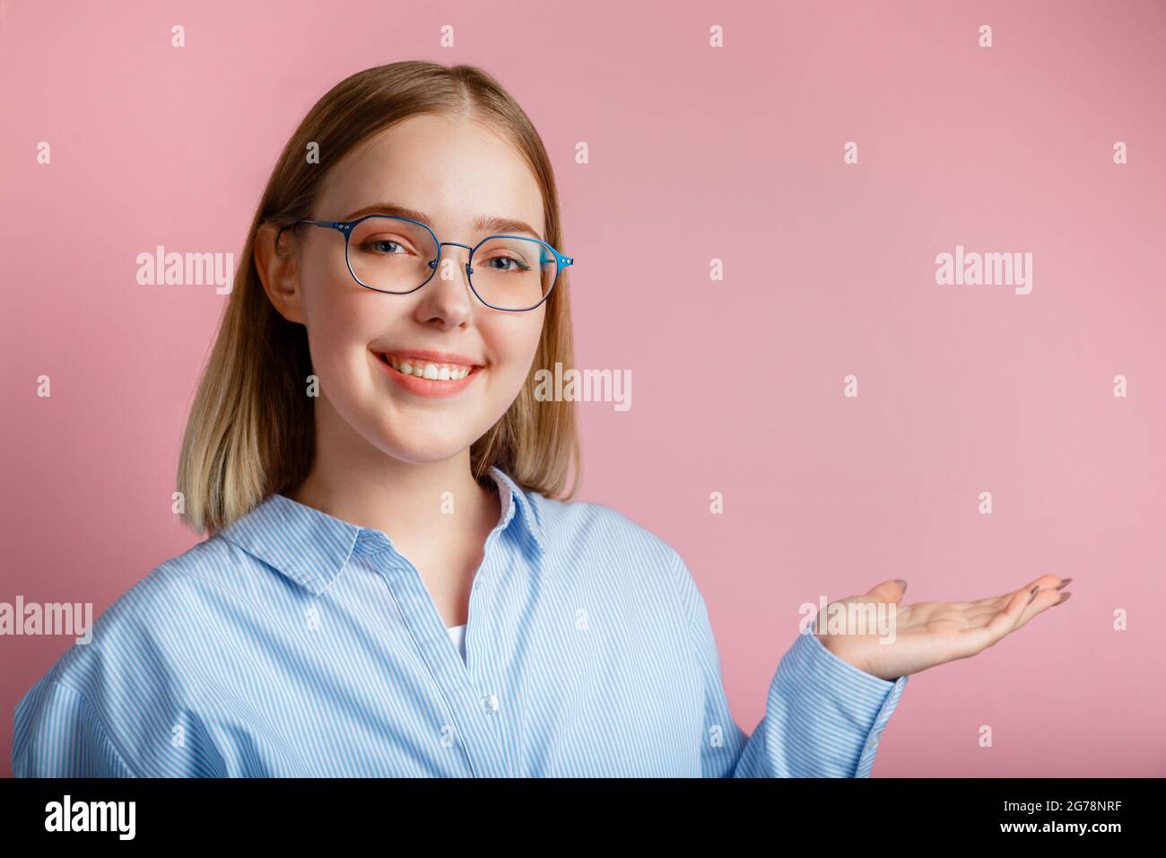 Young business woman or manager in glasses office clothes smiles show side gesture by hand. Teenage girl student wearing glasses shows hand gesture on Stock Photo