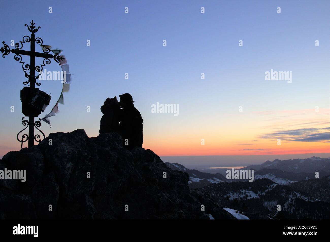 young couple deep embrace, kiss, enjoying the sunrise and the view from the Auerspitz (1811m) towards Chiemgau, to the right of the couple the Wildalpjoch (1725m) behind the Chiemsee, the Kampenwand (1668m) on the far right, atmospheric, Upper Bavaria, Bavaria, Germany , Bavarian Alps, Mangfall Mountains Stock Photo