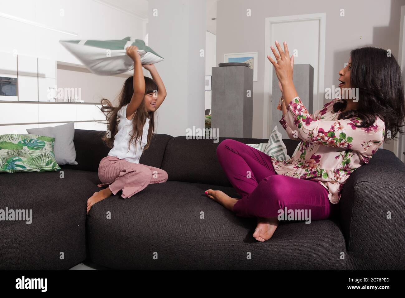 Mother and child have a pillow fight in the living room on the sofa, harmonious, fun, emotional, joyful Stock Photo
