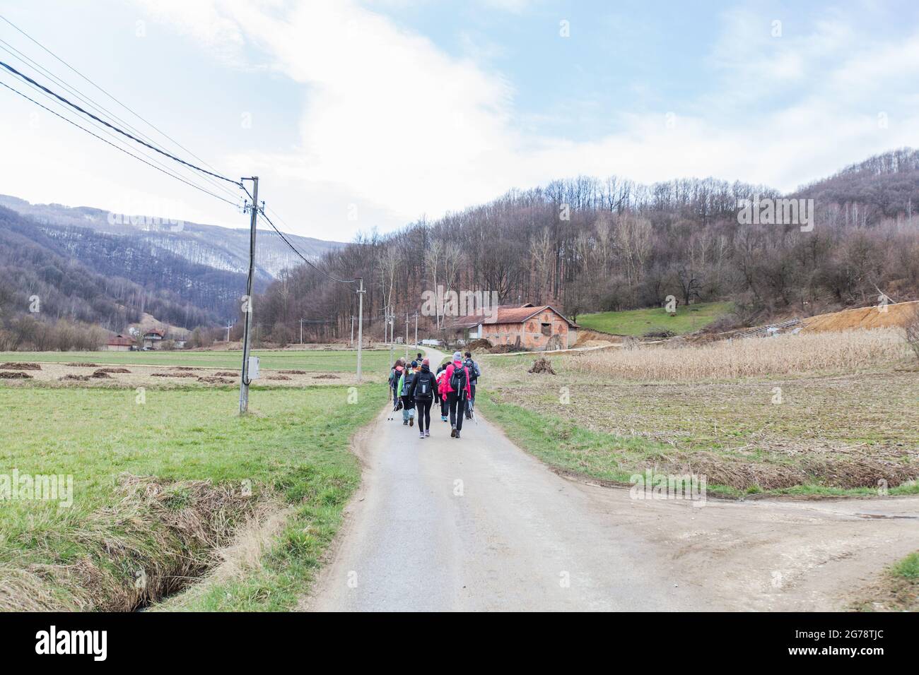 Hiking, Travel, Healthy Lifestyle. Group of active people with backpack walking on a rural road in early spring day. Stock Photo