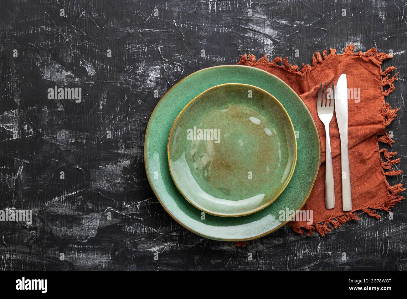 Empty green plate served with knife, fork and table napkin. Mockup template plate for luxury dinner with copy space on dark black concrete table top Stock Photo