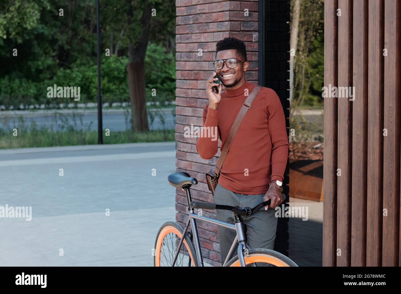 Young African businessman with bicycle phoning in urban environment Stock Photo