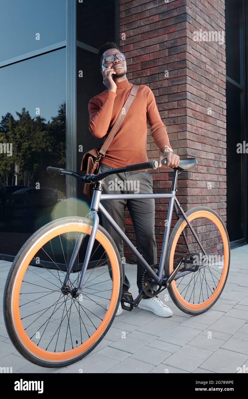 African businessman with bicycle calling on smartphone against building exterior Stock Photo