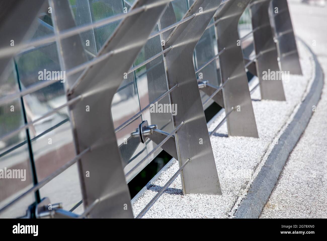 metal turnbuckles fastening of cables with steel rod on pedestrian bridge with stone pebble path and glass barrier for safety close-up details of cons Stock Photo